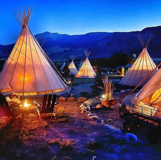 Illuminated tipis glowing at dusk with a mountain backdrop.