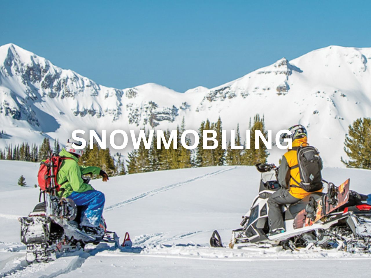 Two snowmobilers pause to admire the snowy mountain landscape.