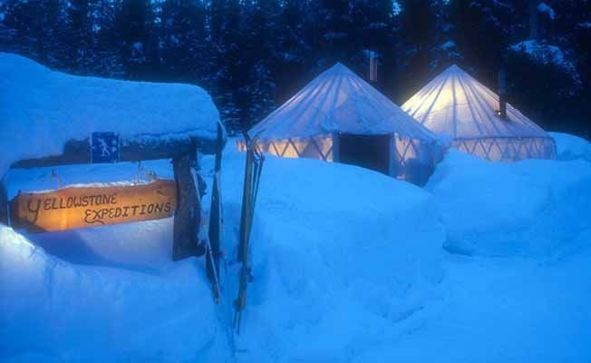 Snow-covered tents illuminated at night with a sign reading "Yellowstone Expeditions."