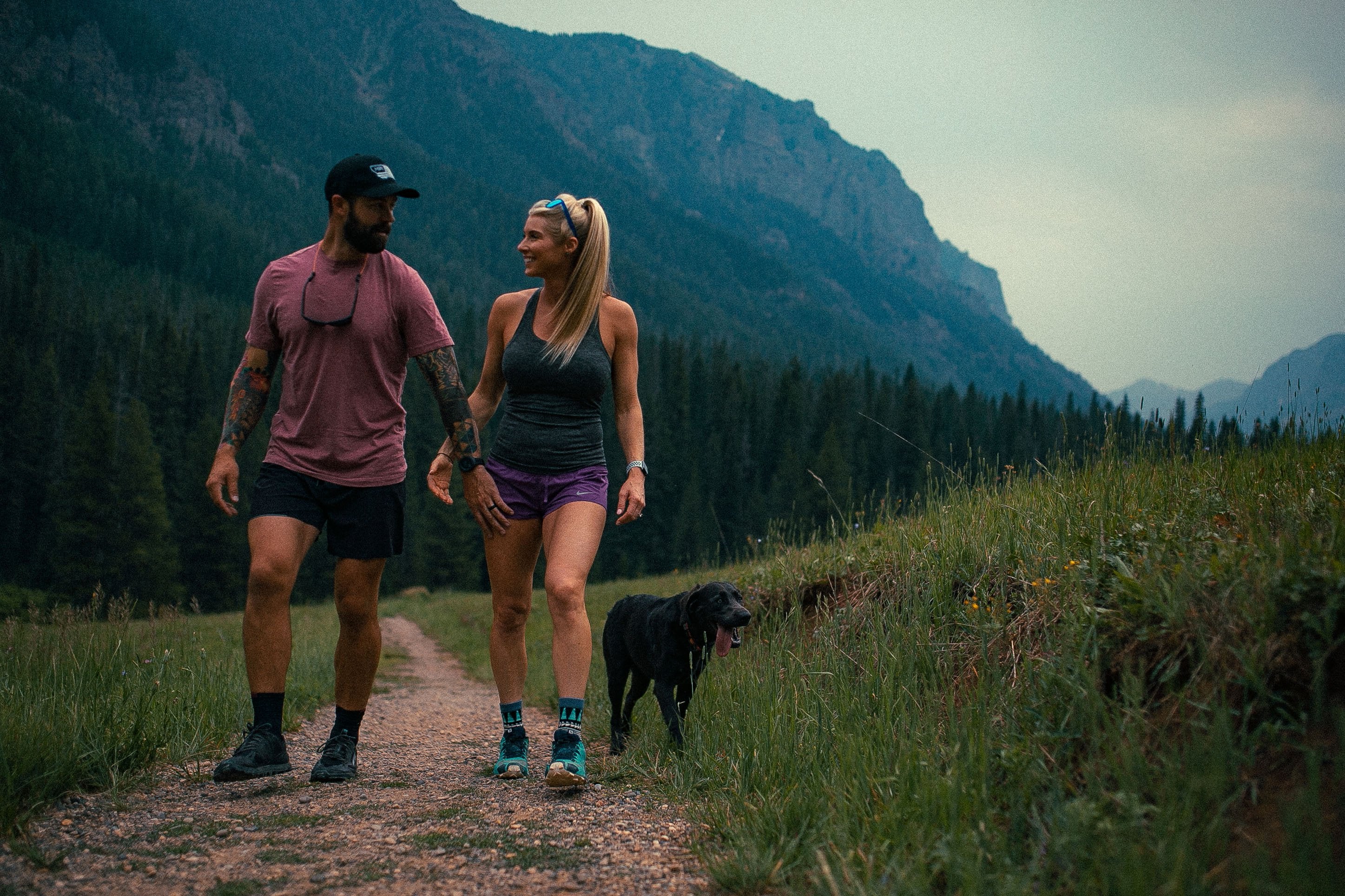 A man and woman stroll along a scenic trail, accompanied by their dog, enjoying a leisurely outdoor experience together.