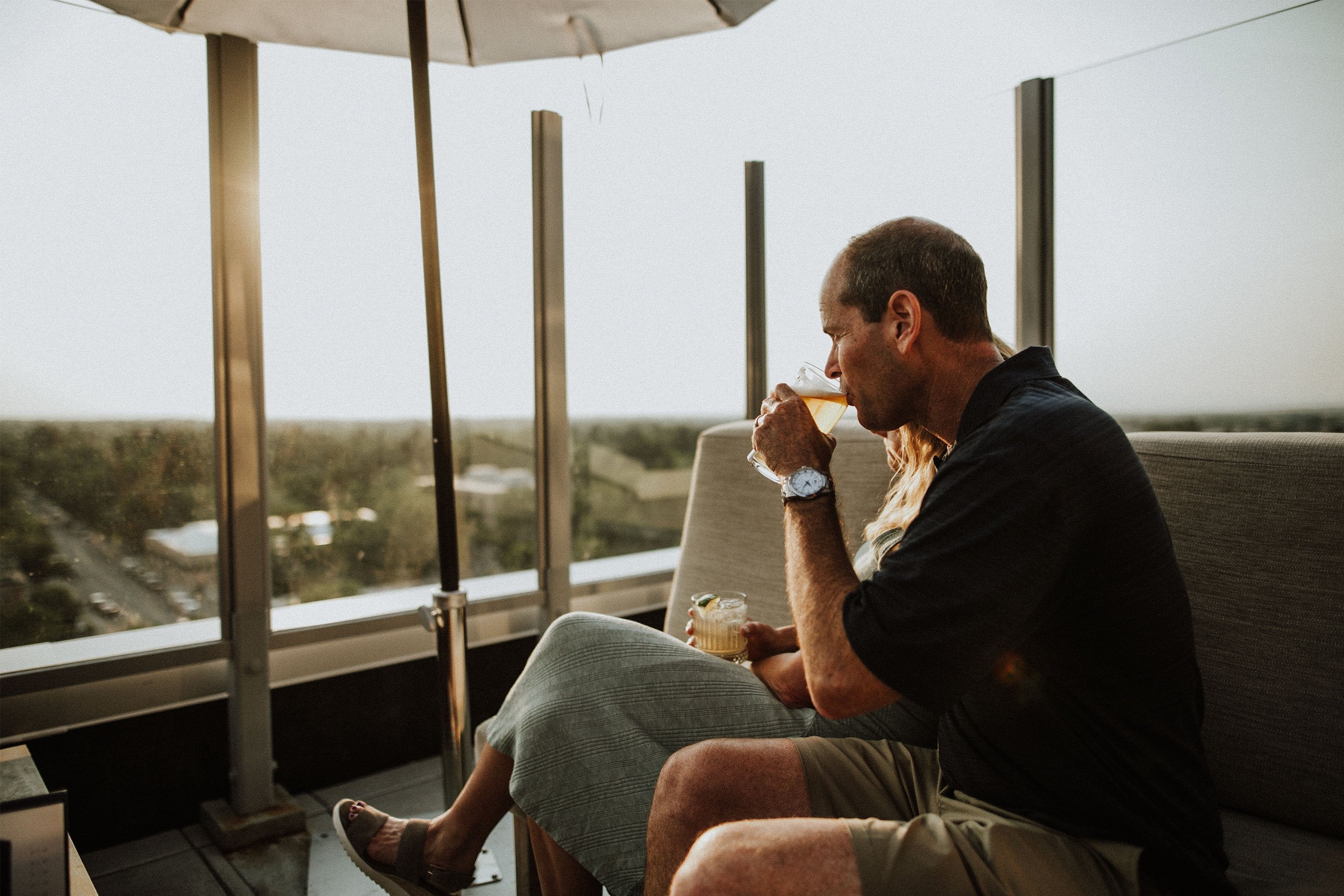 A man and woman relax on a couch, sharing a cozy moment under a colorful umbrella indoors.