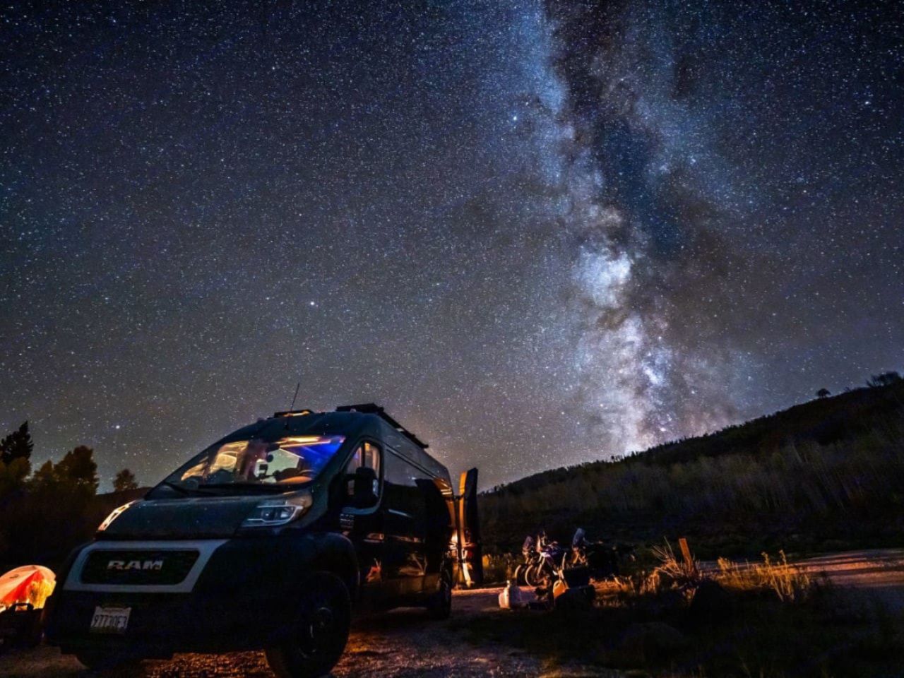 Camper van parked under a star-filled night sky with the Milky Way visible.