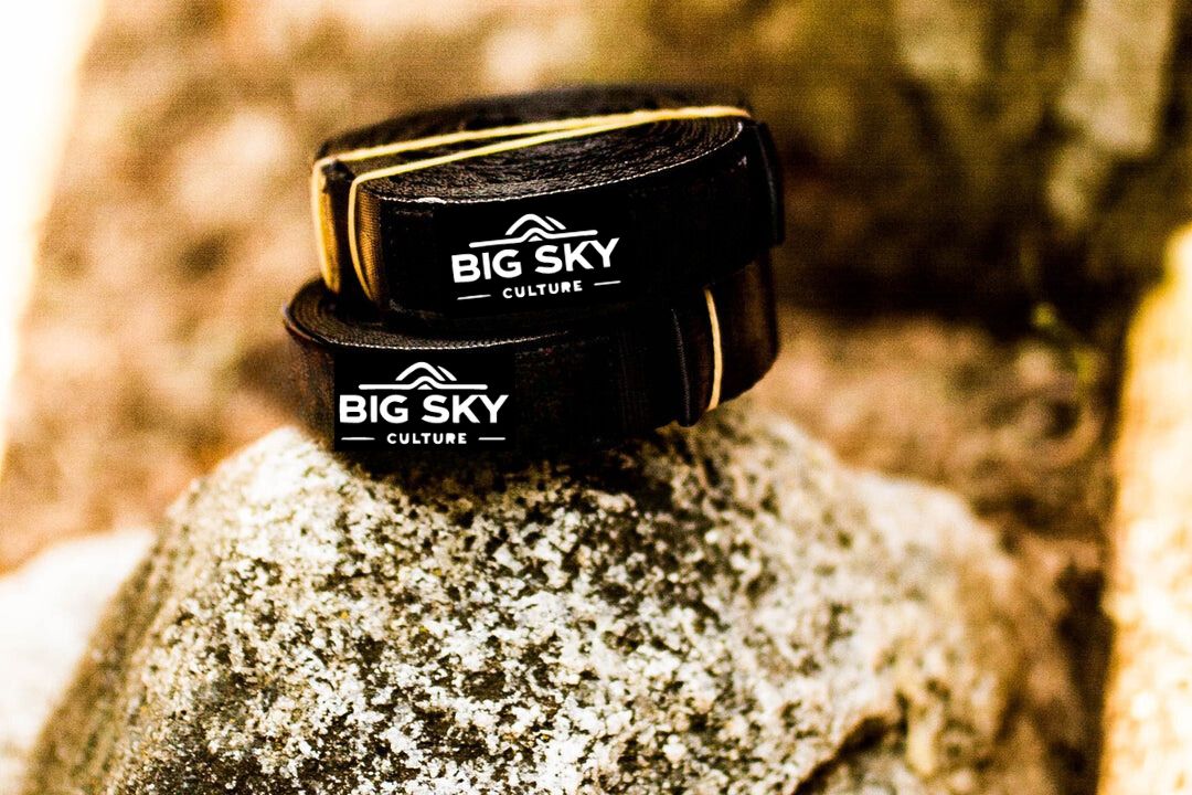 Black leather wristbands featuring the "Big Sky Culture" logo, photographed on a rock, highlighting their outdoor and adventurous appeal.