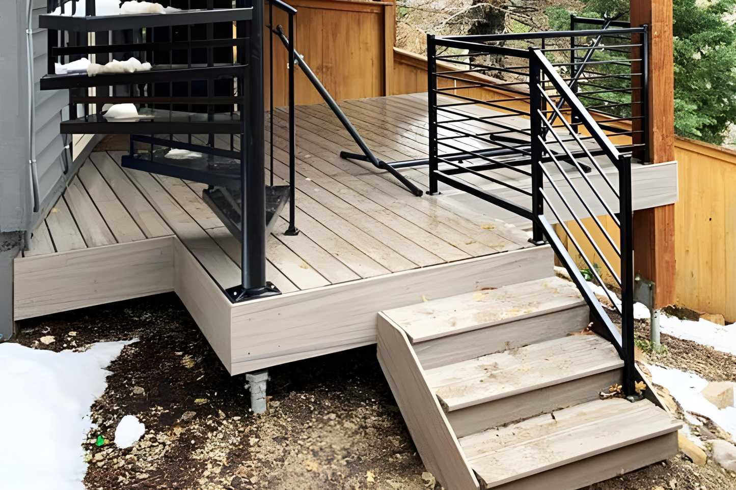 A wooden deck with stairs and railing in front of a white house.