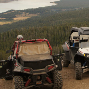 Two ATVs stationed on a dusty road near a calm lake, with picturesque views of nature in the background.