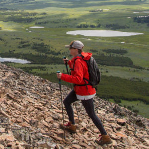 A person trekking uphill on a rugged path, overlooking vast fields and lakes.