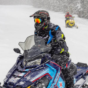 Snowmobile riders navigate a snowy trail during a winter storm.