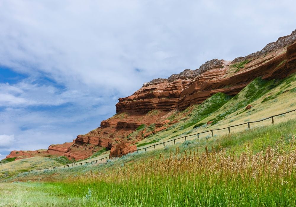 Red rock cliffs with green grassland under a partly cloudy sky.