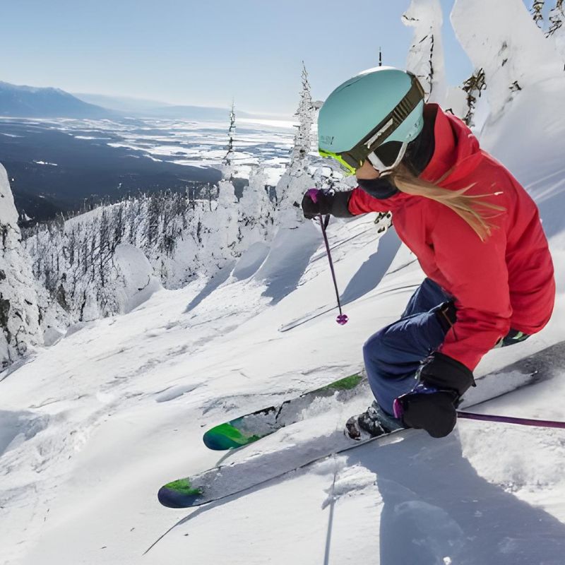 A skier in a red jacket navigates through deep powder on a snowy mountain slope.