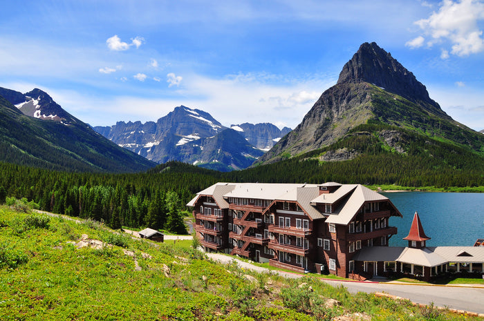 A picturesque lodge set beside a tranquil lake, with dramatic mountain landscapes and dense greenery in the background.