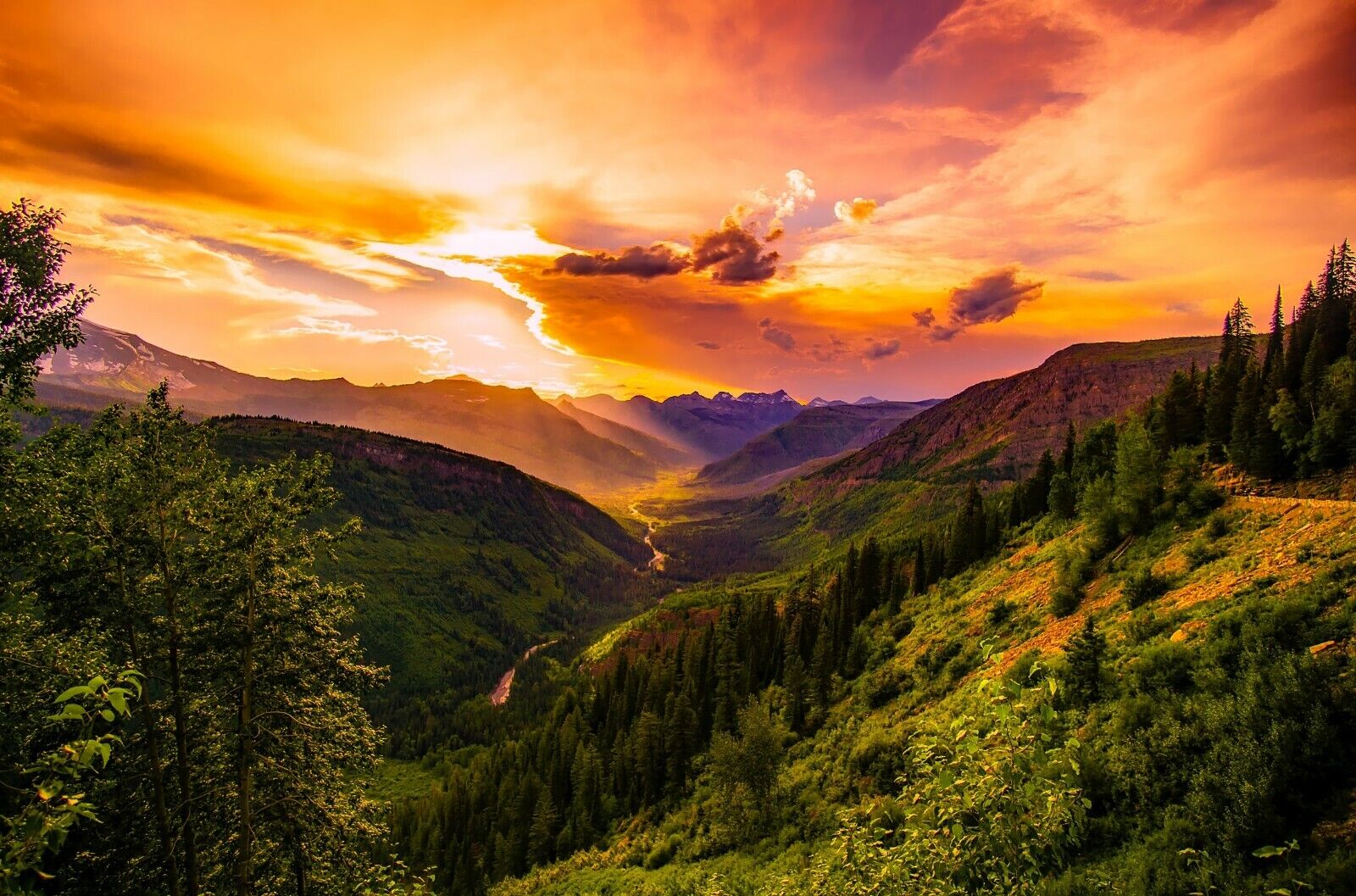 Vibrant sunset over a lush green mountain valley with dramatic skies.