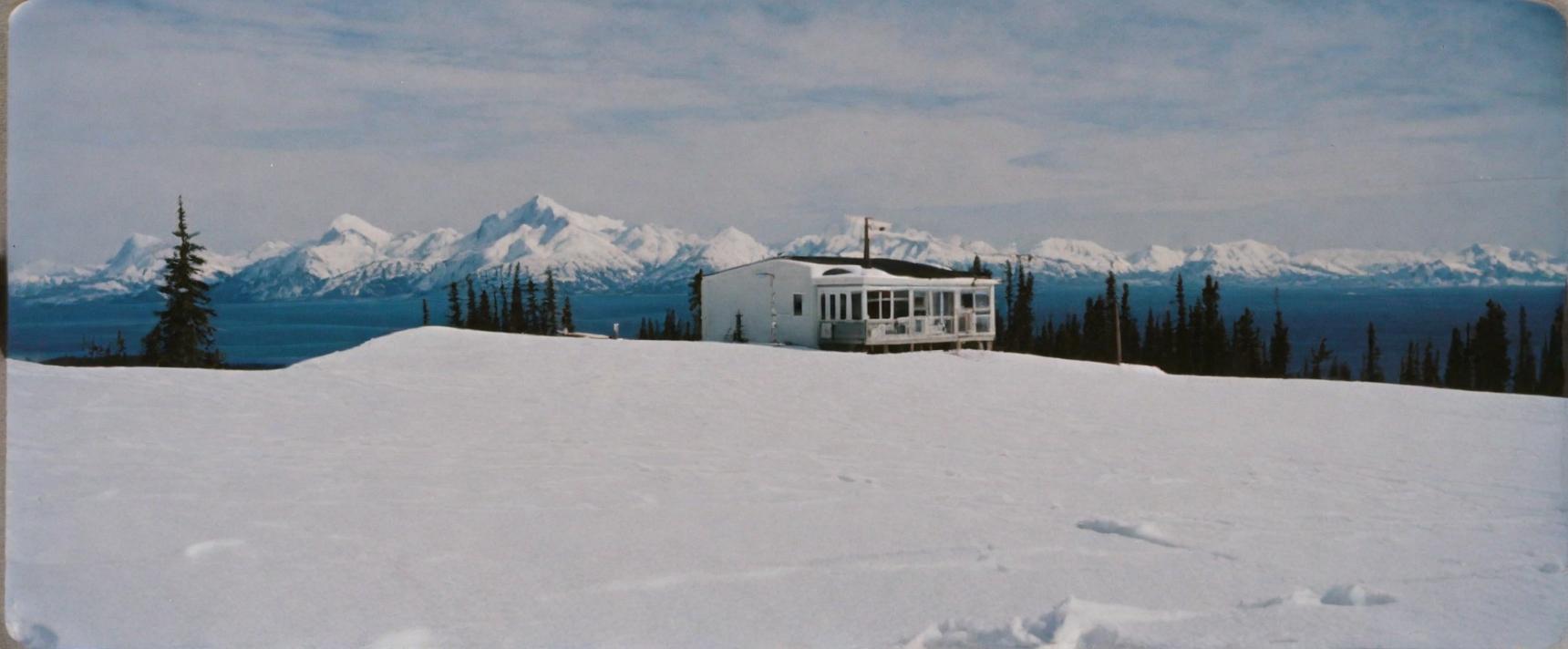 Winter scene featuring a solitary cabin surrounded by snow and distant mountains.