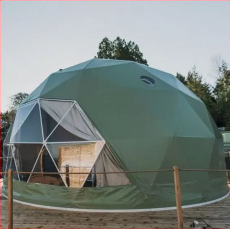 A green geodesic dome tent with large triangular windows, set on a wooden deck. The tent is surrounded by a natural setting with trees in the background, providing a unique and eco-friendly accommodation option.