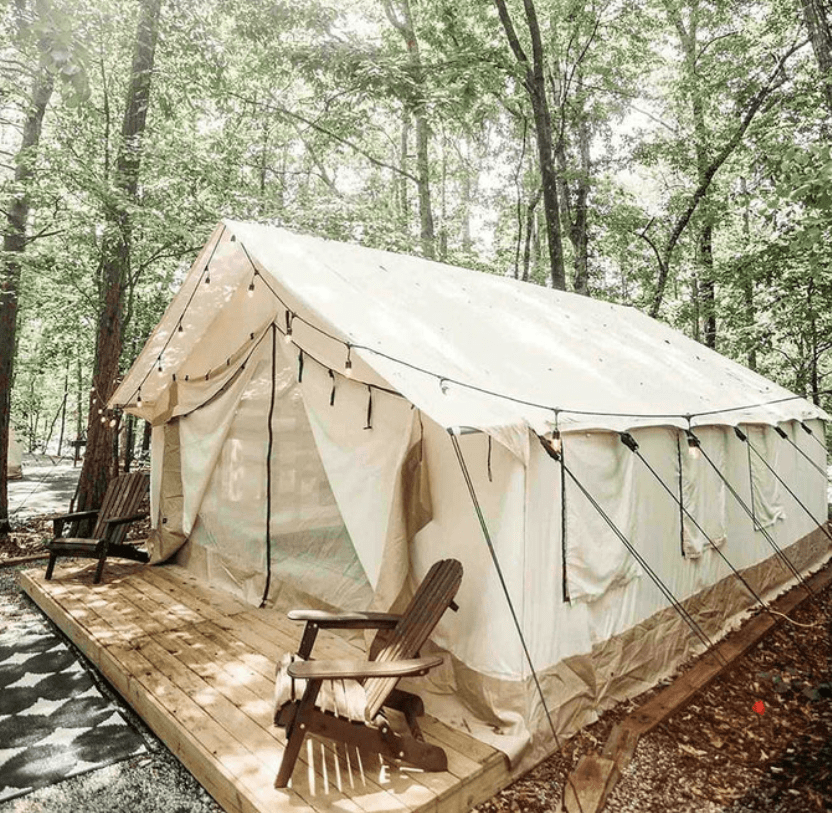 A cozy tent nestled in the serene woods, accompanied by a deck and chairs for relaxation amidst nature's embrace.