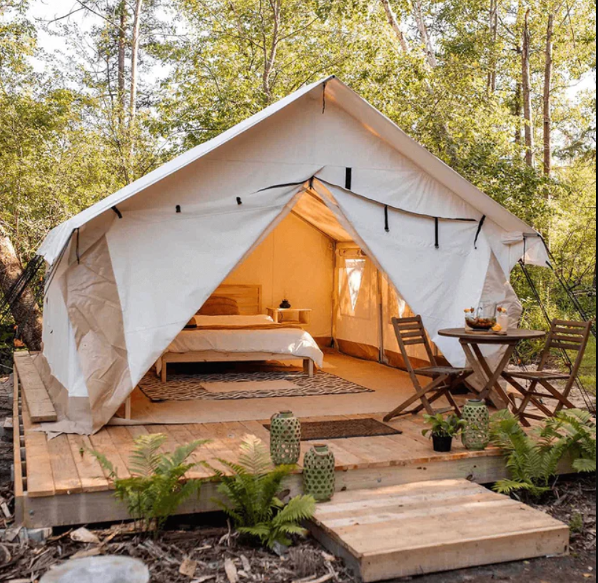 A cozy tent nestled in the woods, featuring a comfortable bed and a table for a serene camping experience.